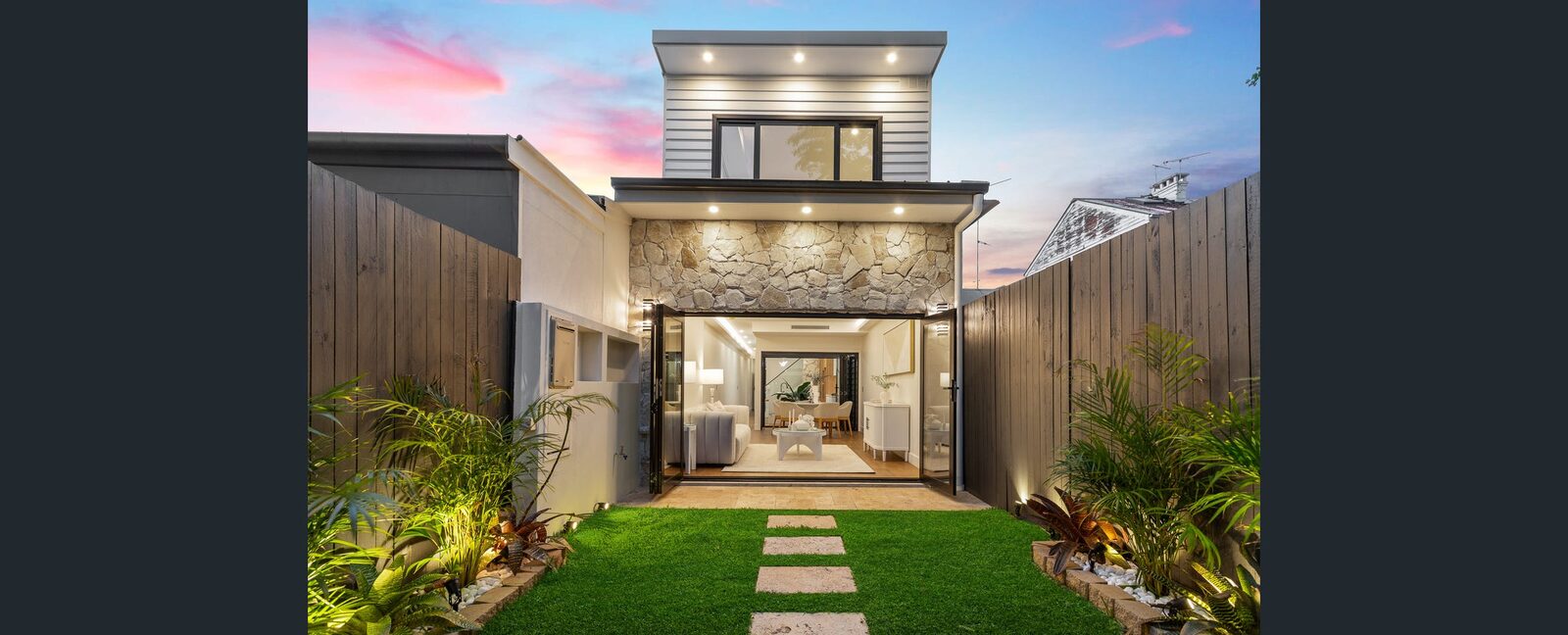 The completed Erskineville home at dusk — a modern rebuilt facade with a stone feature and landscaped frontage