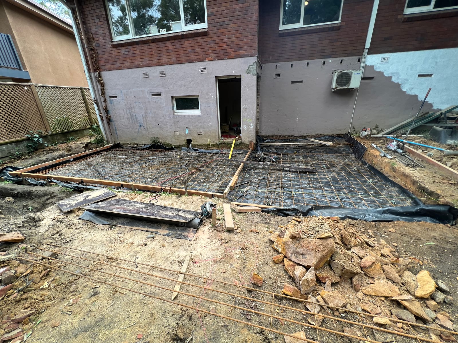 Rebar mesh laid over the excavated footing for the new lower-ground level, against the existing rendered/brick rear wall