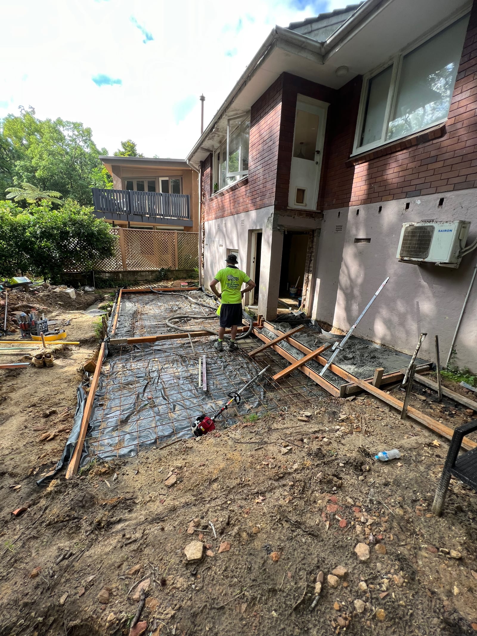 Concrete being poured into the new footing slab, with the existing house and an air-conditioning unit above
