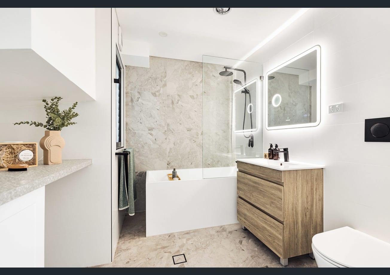 After — The bathroom mid-fitout with tiling, bath and vanity installed but unstyled, and the same bathroom finished with a backlit mirror