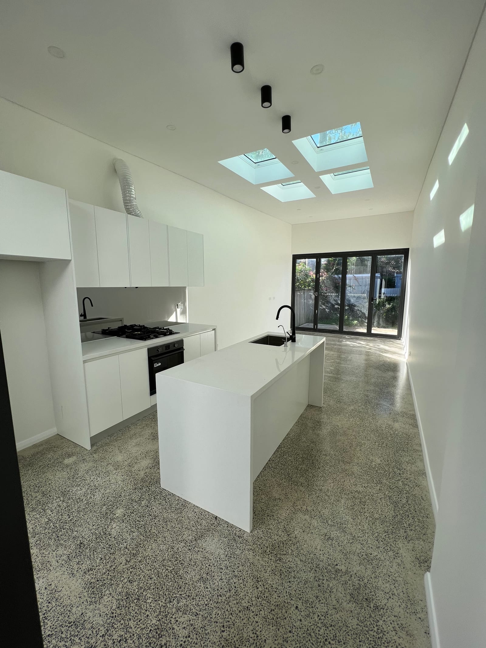 Before — The kitchen and living space during construction with a bare concrete floor and no cabinetry, and the same room finished and furnished